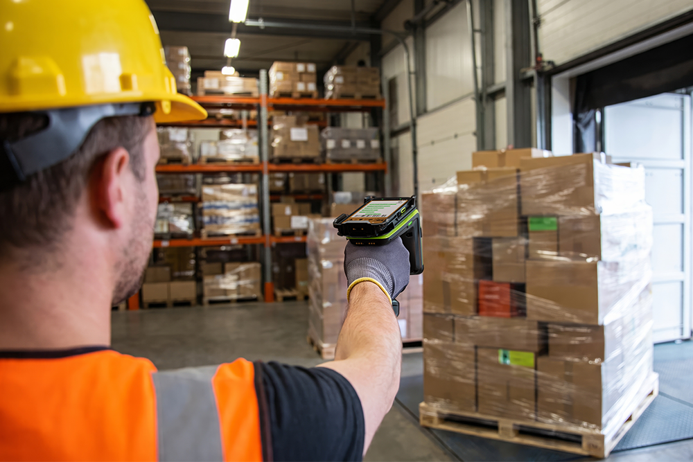 Lagermitarbeiter prüft eine Palette mit Zebra RFD90 RFID-Sled und TC501 Mobilcomputer an der Verladerampe. Lagermitarbeiter scannt eine Palette mit Zebra RFD90 RFID-Sled und TC501 Mobilcomputer an einer Verladerampe